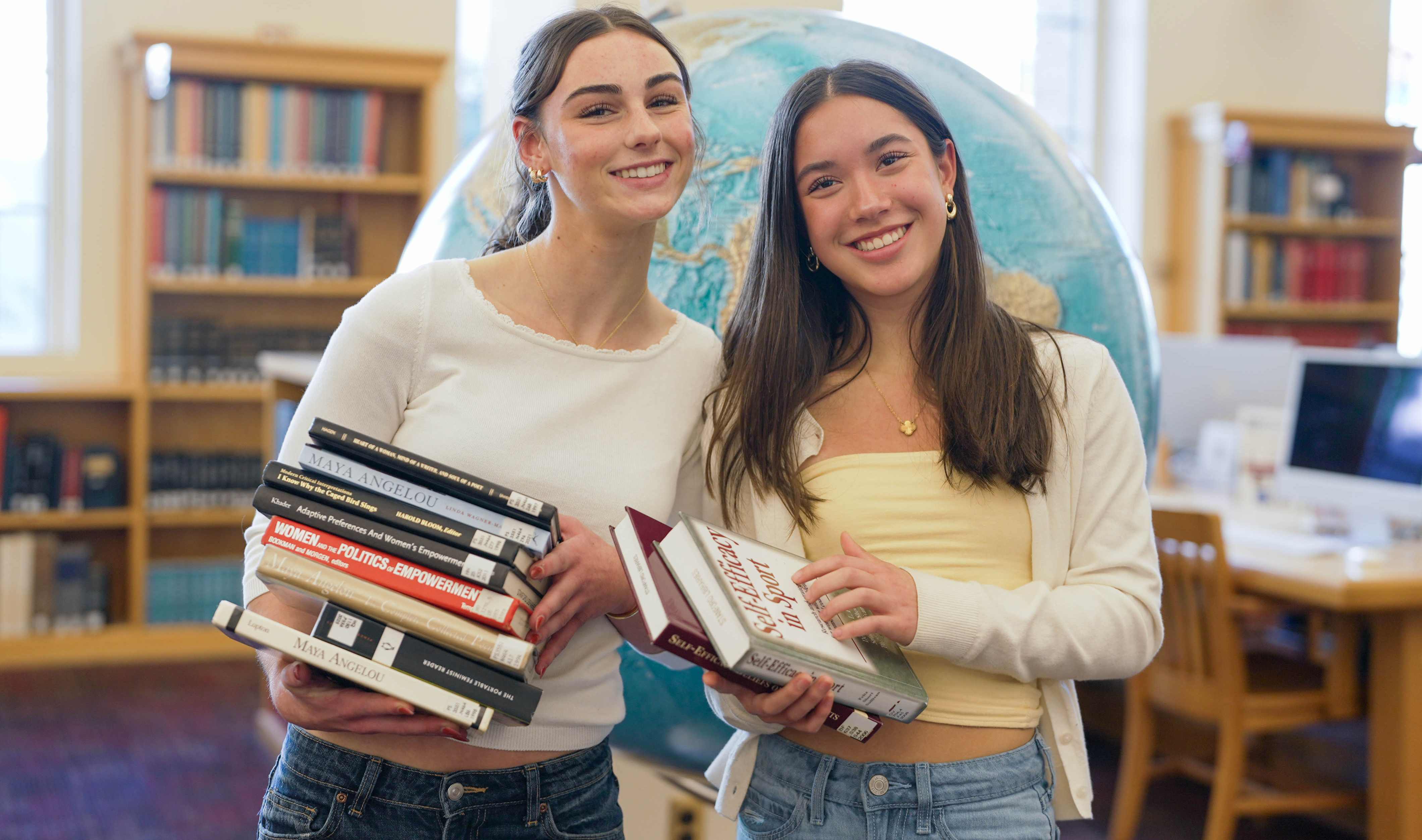 Two HS students in the library pose for a photo in front of a giant globe.